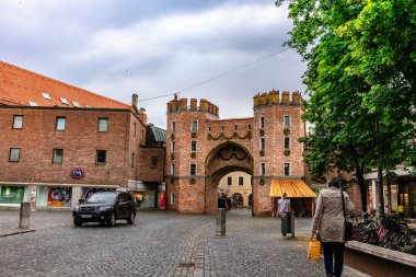 Landshut, Almanya - 24 Temmuz 2023: Eski kasabadaki ortaçağ şehir kapısı Landtor 'u restore edildi. Eski kırmızı tuğla kapı ve yağmurlu yaz gününde sokaklarda yürüyen insanlar, Landshut, Almanya
