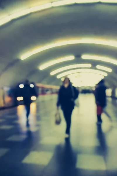 Lens blur image of a subway with silhouettes of moving people.