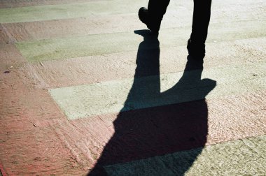 Pedestrians walking on zebra crossing throwing hard black shadow oh the road.
