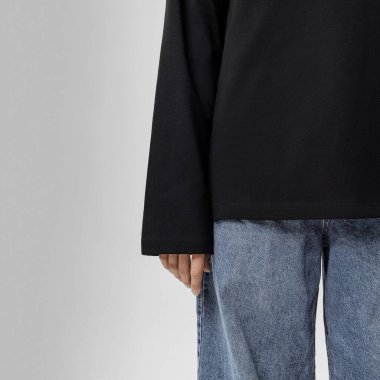 Stüdyoda kadın eli ve alt gövde yakın çekim siyah uzun kollu üst ve mavi kot pantolon giyerek.