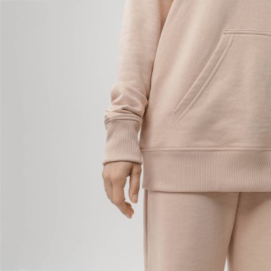 Bej bir kapüşonlunun cebinde dinlenen, yumuşak kumaş dokusunu ve rahat bir gecelik tasarımını ön plana çıkaran bir kadının yakın çekimi..