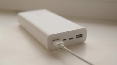 Dış batarya güç bankası pencere kenarında duran akıllı telefonu şarj ediyor. Gösterge yanıp sönüyor. Yüksek kalite 4k görüntü.