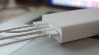 Harici batarya güç bankasına bağlı dört usb kablosu dizüstü bilgisayarda bulunan akıllı telefonu şarj ediyor. Gösterge yanıp sönüyor. Yüksek kalite 4k görüntü.