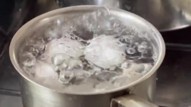 Görünür buhar ve su kabarcıkları olan gümüş bir tencerede yumurta kaynatmak. Yüksek kalite 4k görüntü.