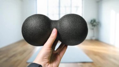 Geniş pencereli ve ahşap zeminli parlak bir odada, özel köpükten yapılmış siyah bir yer fıstığı masaj topu. Yüksek kalite 4k görüntü.