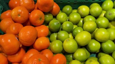 Canlı mandalinalar ve limonlar, yerel bir markette satın alınmaya hazır yeşil sandıklarda renkli bir ekran oluşturuyor.