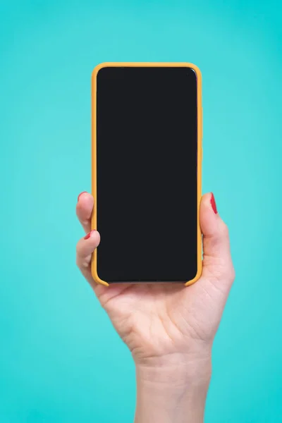 Tek El, siyah ekranlı yeni akıllı telefonu dikey görüntüde mavi arkaplanda tutuyor. Dikey pozisyonda kadın elleri. Yüksek kalite fotoğraf
