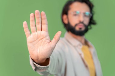 Yeşil arka planda gözlük takan yakışıklı genç adam avucunun içi gibi şarkı söylemeyi kesiyor. Yüzünde olumsuz ve ciddi bir jest olan uyarı ifadesi. Yüksek kalite fotoğraf