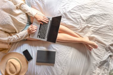 Manzaralı kız yatakta oturup bir seyahat ve otel ayarlamayı planlıyor. Postaları kontrol etmek, internette sörf yapmak ya da çalışmak, bilgisayarından alışveriş yapmak. Rahat bir ev. Uzayı metin için kopyala. Yüksek kalite fotoğraf