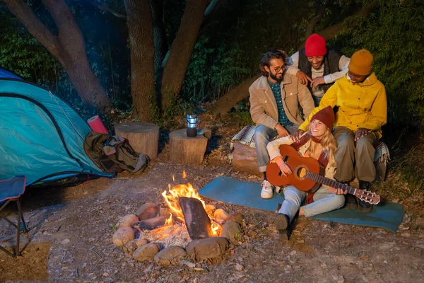 Friends around campfire at night playing guitar music and enjoying the nature. High quality photo