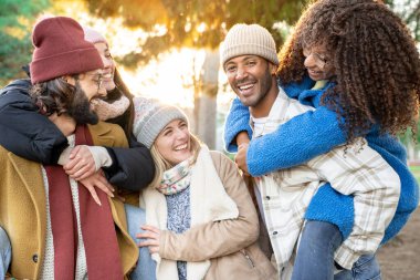 Multiracial young group of happy friends having fun in the park. Students laughing and having fun together, smiling people, hugging, piggyback. High quality photo