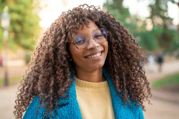 Young african woman portrait, face of female student smiling looking to the camera in the campus. Afro hair, wearing blue jacket and glasses. High quality photo