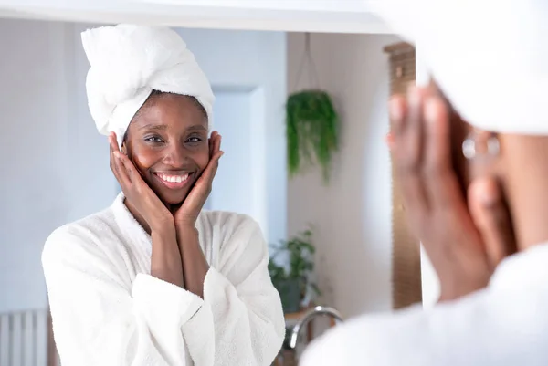 Black woman applying cream morning skin care routine, girl looking to camera touching face treating for nourishing and moisturizing effect. High quality photo