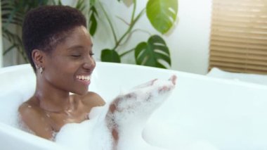 Woman relaxing blowing soap bubbles while relaxing in foam bath at home. High quality 4k footage shot on RED camera in slow motion.