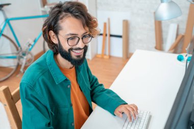 Modern ofiste çalışan genç yaratıcı bir adam. Stüdyoda bilgisayarla yeni bir proje üzerinde çalışıyor. Ofiste otururken, yapılan işten memnun. Yüksek kalite fotoğraf