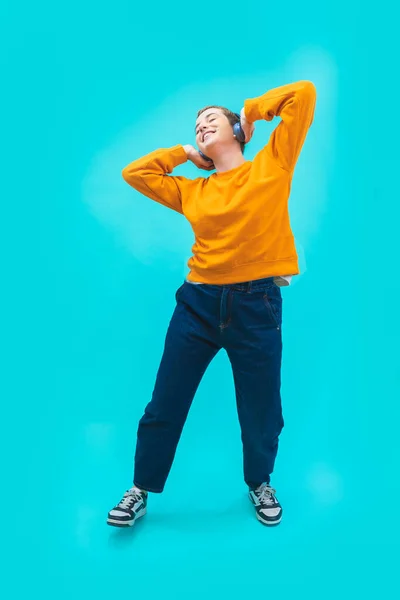 Cool young woman listening music dancing isolated on blue background with happiness. Concept of joy, pleasure, sales, fashion and youth. Vertical shot copy space for text