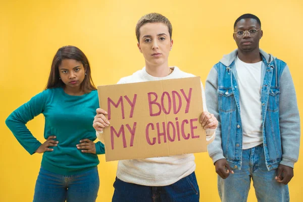 Multi ethnic students holding banner showing message abortion. Isolated on background, text copy space. Women rights, activism, feminist, girl power, stop patriarchy, 8m concept.