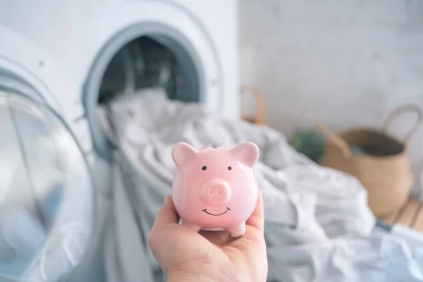 Energy and electricity crisis, money savings piggy bank. Reduce household bills expenses, washing machine in the background
