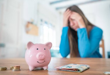 Woman with pink piggy bank worry and sad about money and household finances. Family savings and home economy