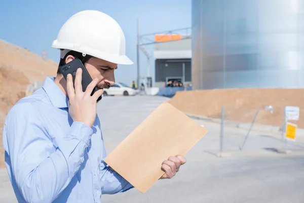 İnşaat mühendisi inşaat alanındaki inşaat alanında duran akıllı telefonlu amirle iş görüşmesini inceliyor. Ehliyetleri, planları, denetimi, denetlemesi var. Uzayı metin için kopyala. Yüksek kalite fotoğraf