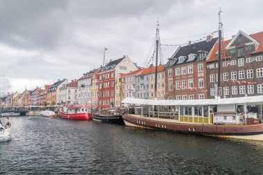 Kopenhag, Danimarka - 26 Temmuz 2022: Bulutlu bir günde renkli binalarla Nyhavn Kanalı 'nın güzel manzarası. Liman ve çizgiler parlak renkli ev ve barlarla kaplı..