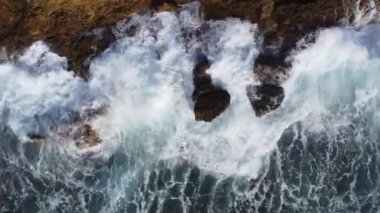 Güçlü dalgaların yukarıdan aşağı görüntüsü kayalık kıyıya çarpar. Dalgalar denizdeki kıyı kayalarına çarpar..