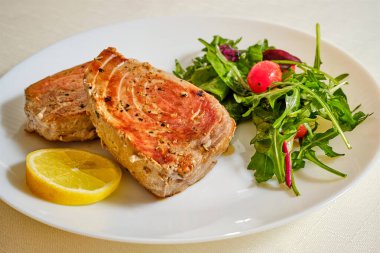 Tasty tuna fish steak on white plate with salad