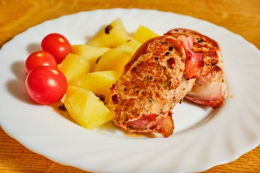 Tasty pork fillet in ham with boiled potatoes and red tomatoes