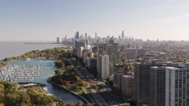 Aerial drone footage of the skyline of downtown Chicago in the distance with boats docked in Belmont Harbor and highrise buildings along Lake Shore Drive in the foreground.