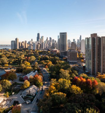 Chicago, IL - October 19th, 2022: Bright red and yellow fall tree foliage begins to appear in the Lincoln Park neighborhood as sunlight shines between high-rise buildings casting shadows on the area.