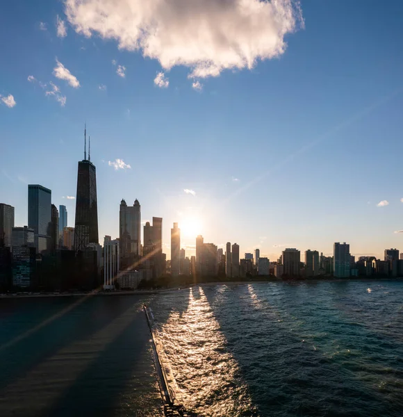 Beautiful downtown Chicago skyline aerial drone photograph during the Chicago henge or autumn equinox as the sun sets between high-rise buildings casting a yellow glow and long shadows over the lake.