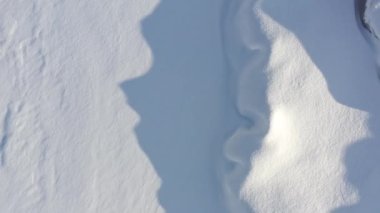 Aerial drone top down flying low over snow drifts along Lake Michigan with cold blue jagged shadows landing on the adjacent snow.