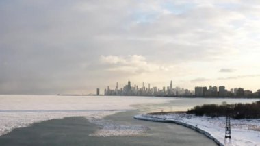 Rising up aerial drone footage of the Chicago skyline from above a partially frozen Lake Michigan with winter scenes and people walking on the pier and shoreline below.