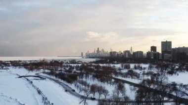 Montrose sahilinin üzerinde uçan hava sahneleri ve zemini kaplayan Kriket Tepesi ve üzerinde bulutlu günbatımı gökyüzü olan Chicago silueti..