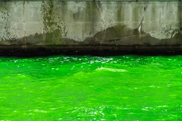 聖パトリックの休日のための毎年恒例の川の染色イベントの間にコンクリート海岸線に打ち寄せる波とシカゴ川の明るい緑の水の写真を閉じます — ストック写真