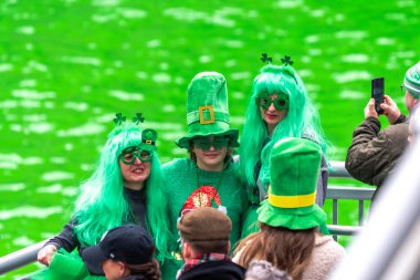 Chicago, IL - 11 Mart 2023: Aralarında yeşil saç ve cüce şapkaların da bulunduğu bir grup insan, şehir merkezindeki yeni boyanmış yeşil nehrin önünde fotoğraf çektirmek için poz veriyor..