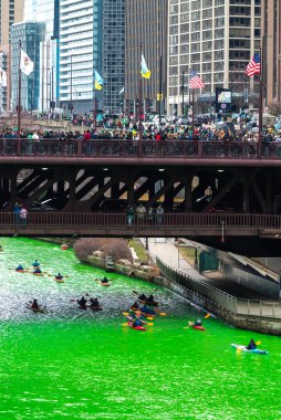 Chicago, IL - 11 Mart 2023: DuSable Köprüsü 'nün altından bir kano turu geçerken, insanlar her yıl düzenlenen St. Patrick Günü' nde Michigan Bulvarı 'ndan yukarıdaki yeşil nehir boyama etkinliğini izliyorlar..