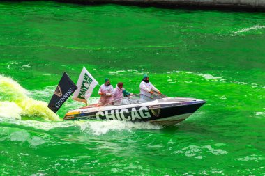 Chicago, IL - 11 Mart 2023: Tesisatçı 130 Birlik Guinness bira teknesi rüzgarda dalgalanan bayraklarla taze boyanmış Chicago Nehri 'nin parlak yeşil sularında bir uyanış yarattı.