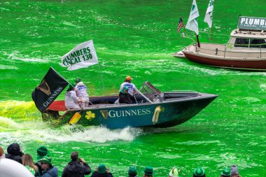 Chicago, IL - 11 Mart 2023: Tesisatçı 130 Birlik Guinness bira teknesi rüzgarda dalgalanan bayraklarla taze boyanmış Chicago Nehri 'nin parlak yeşil sularında bir uyanış yarattı.