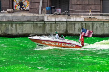 Chicago, IL - 11 Mart 2023 Dunkin Donuts sponsorluğunda Chicago Nehri 'nin açık yeşil sularında yüzen tekne rüzgarda dalgalanan bayraklarla bir uyanış yarattı..