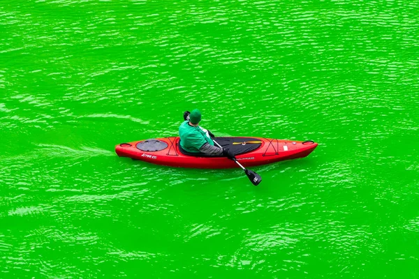 シカゴ 2023年3月11日 ライフジャケットの上に緑のシャツを着た赤いカヤックの男が 聖パトリックの日のイベントで明るい緑の川の光景を見てパドルを休みます — ストック写真