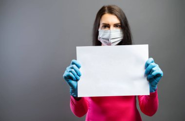 Tıbbi maskeli ve eldivenli kadın ellerinde protesto işareti olarak boş kağıt gösteriyor. Bir kağıt parçasına odaklan. Korona COVID-19 ve SARS Cov 2 enfeksiyonlarını önle, boşluğu kopyala