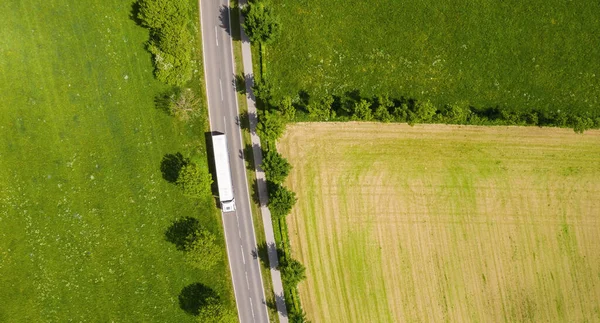 Aerial view of two lane road through countryside and cultivated fields with white truck. Drone shot and copy space for text