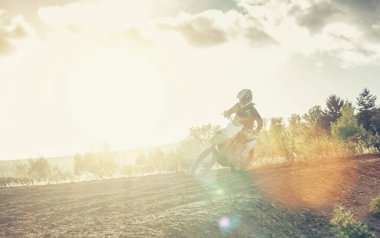 Ekstrem Motocross MX yarışçısı gün batımında toprak yolda hızlanıyor