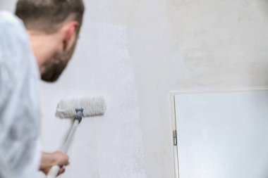 Boyacı beyaz renkli bir odanın duvarını boyamak için boya silindiriyle çalışıyor. Bunu kendin yap konsept görüntü