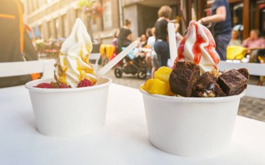 İki dondurulmuş yoğurt, üzerinde browni ve meyve sosu olan bir restoran masasında.