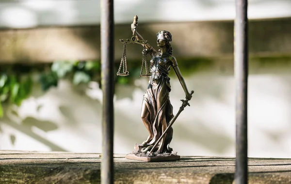The Statue of Justice - lady justice or Iustitia / Justitia the Roman goddess of Justice against a jail grid