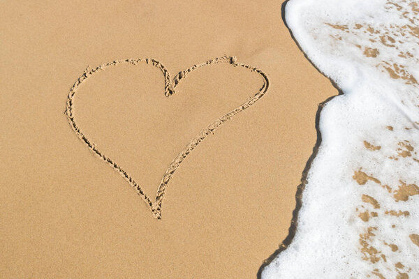 Heart drawn on the beach sand with sea foam and wave