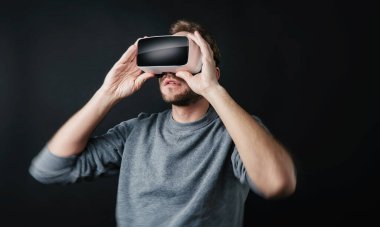 Sanal gerçeklik gözlüğü takan genç adam siyah arka planda VR kulaklık takıyor