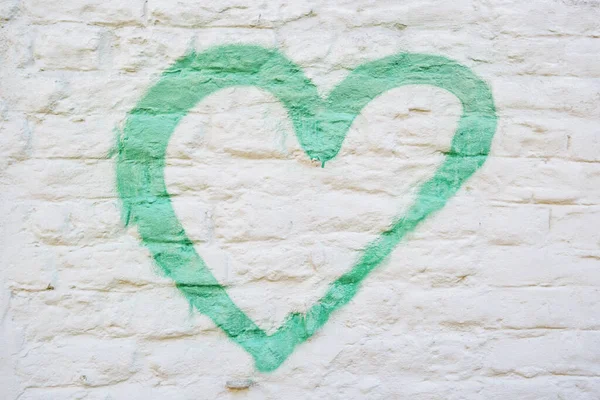 A green heart painted on a distressed white brick wall.